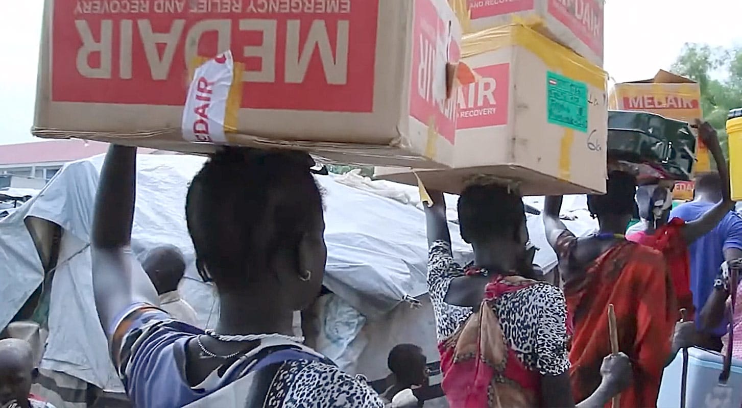 A line of individuals carries Medair food boxes, illustrating the delivery of essential aid to those in need.